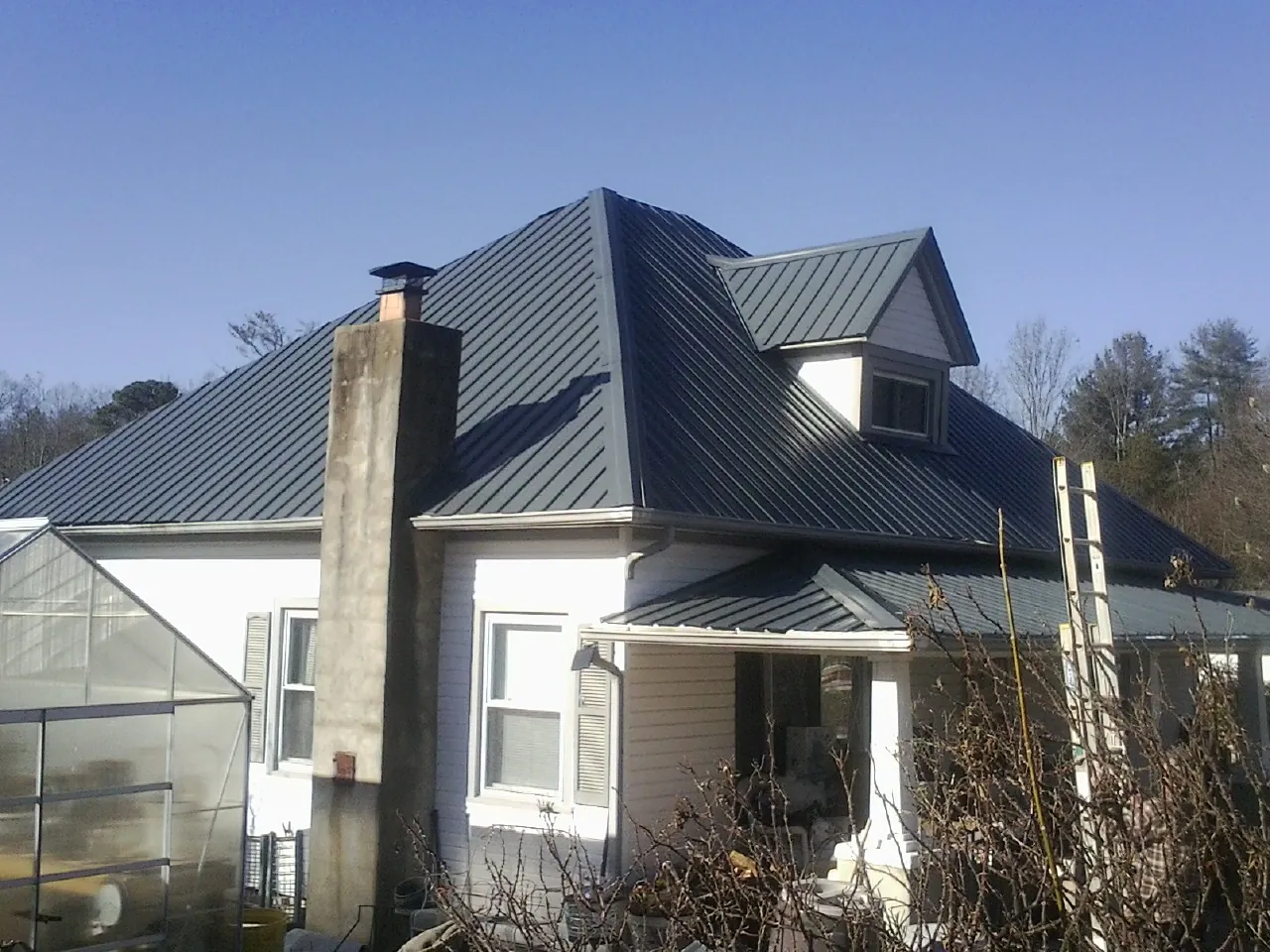 Dark blue standing seam metal roof on a white farmhouse with dormer — Slate & Tile Roof Repair by Roofing Brothers in East Smithfield