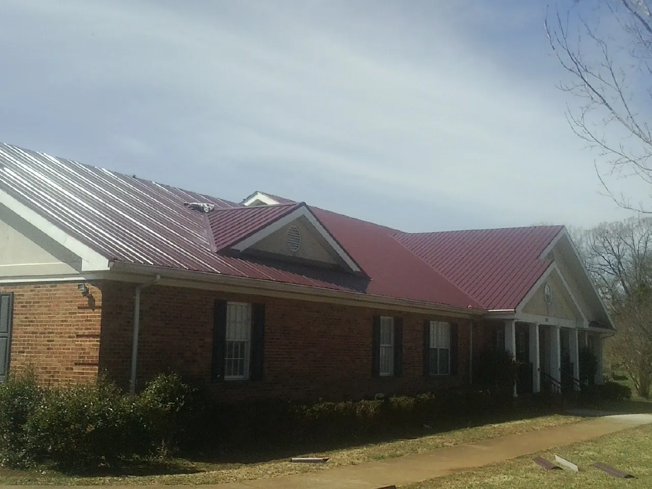 Red metal roof with gabled entries on a long brick building, from a Hail Damage Roof Repair job in East Smithfield