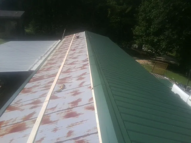 Old rusted panels beside newly installed green metal roofing — Wind Damage Roof Repair by Roofing Brothers in East Smithfield