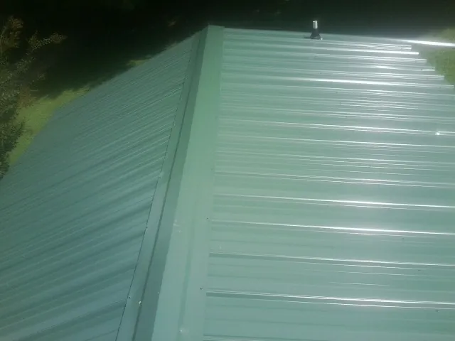 New green metal panels meeting at the ridge of a roof — Flat Roof Repair work by our crew in East Smithfield