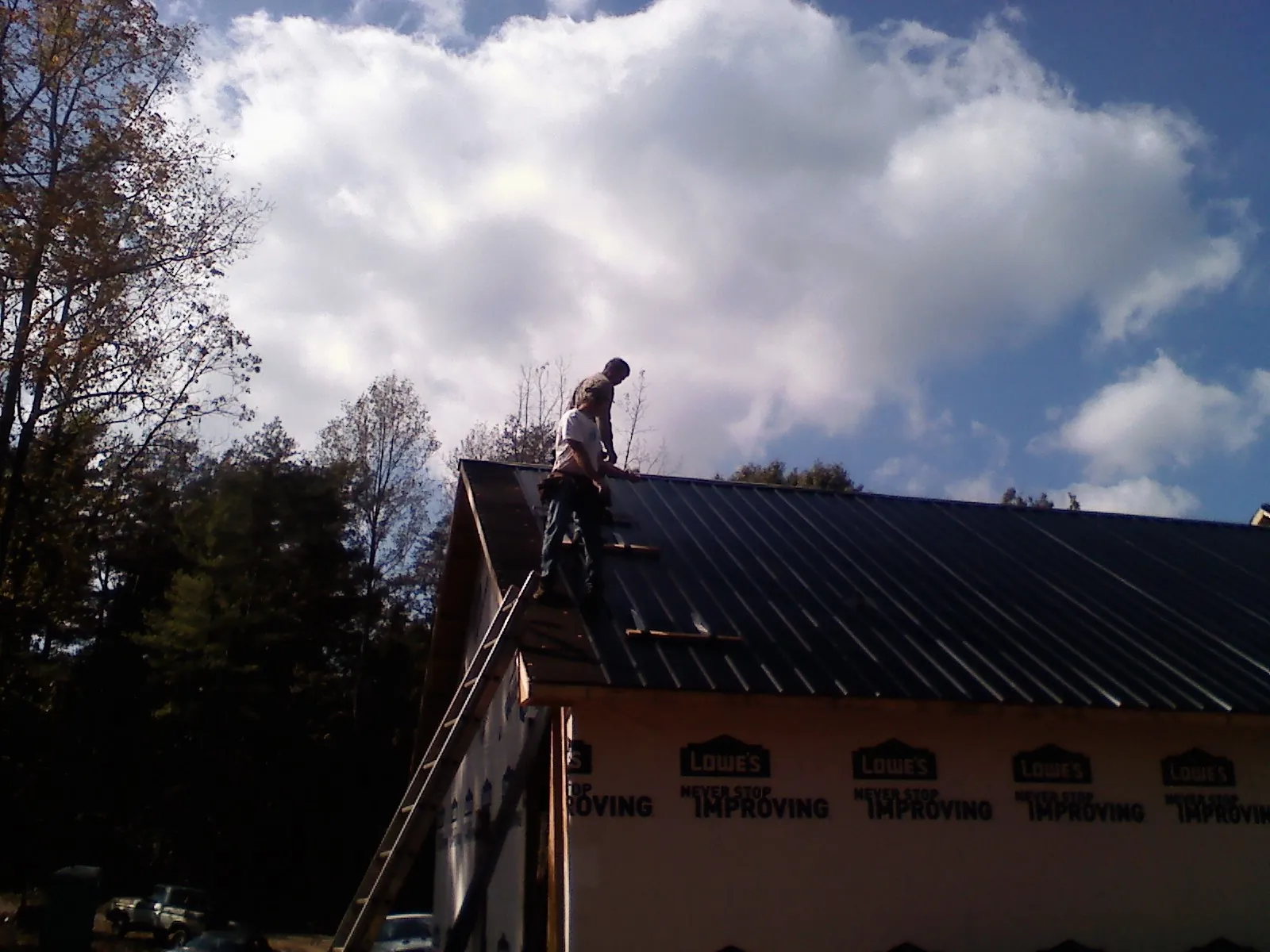 Roofer fastening dark metal panels high against a cloudy sky, from a Roof Inspection job in East Smithfield