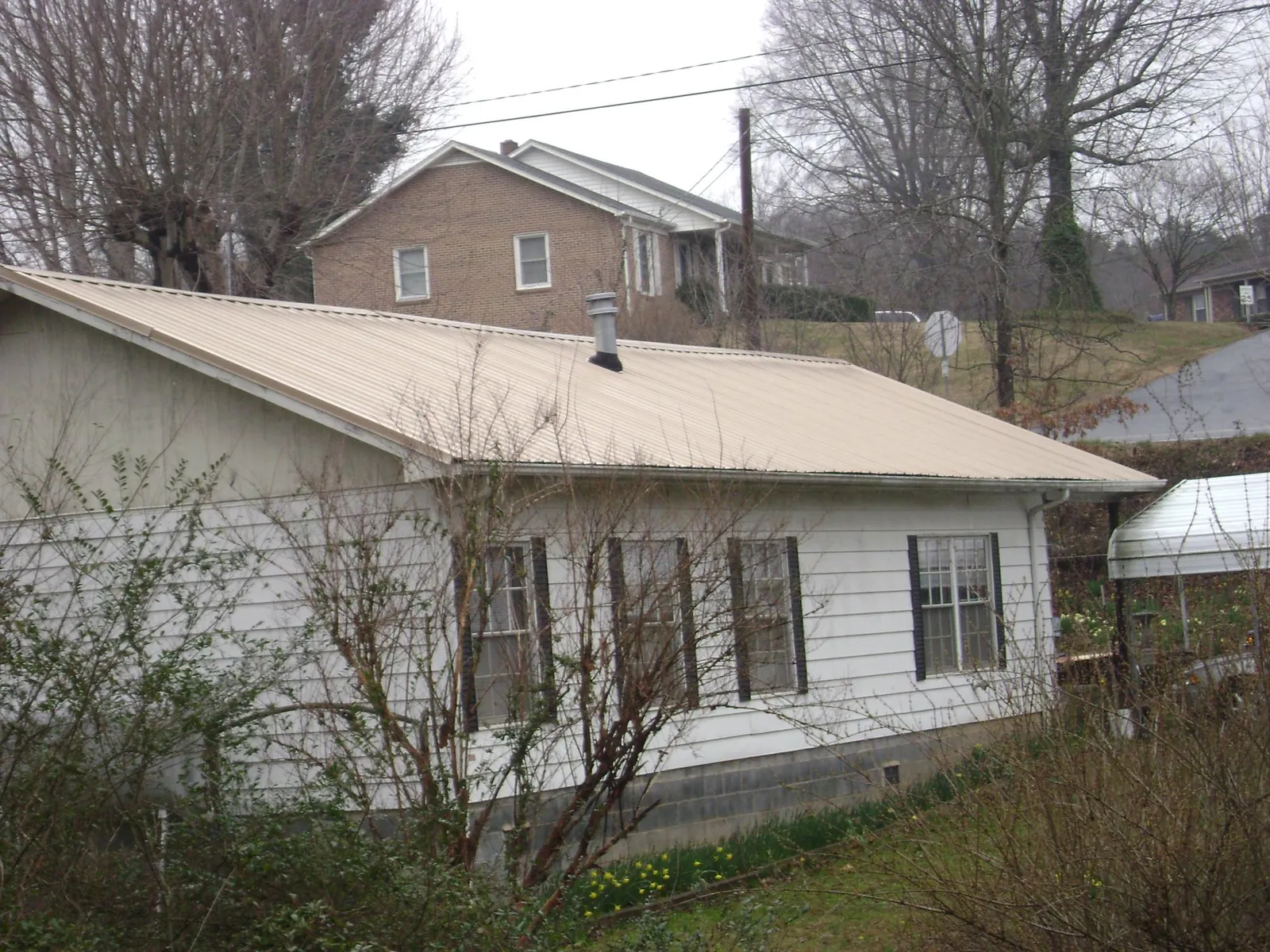 Tan metal roof on a white sided house set into a hillside — Commercial Roofing by Roofing Brothers in East Smithfield