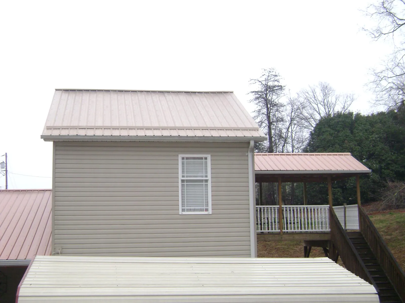 Tan metal roofs on a two story addition and attached porch, from a Roof Replacement job in East Smithfield